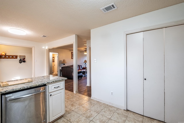 kitchen featuring light stone counters, a textured ceiling, light tile patterned floors, dishwasher, and white cabinets