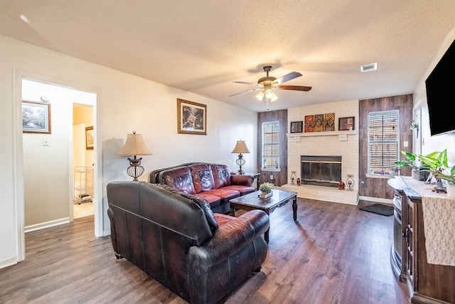 living room with hardwood / wood-style flooring, ceiling fan, a brick fireplace, and a textured ceiling