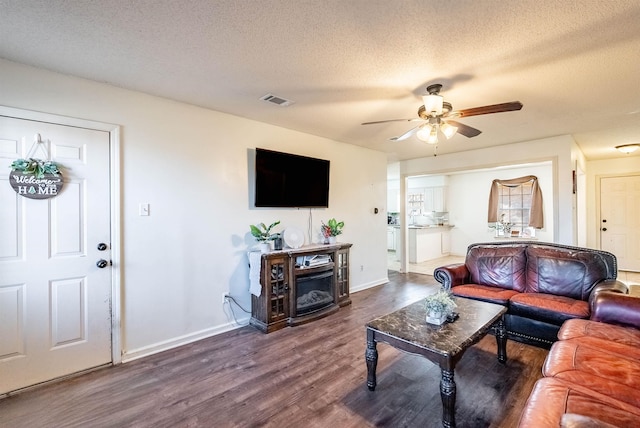 living room featuring ceiling fan, dark hardwood / wood-style flooring, a textured ceiling, and a fireplace