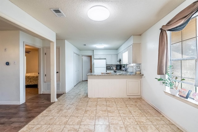 kitchen with white cabinets, white fridge, kitchen peninsula, light stone countertops, and a textured ceiling