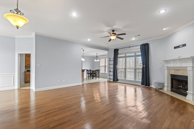 unfurnished living room with a tiled fireplace, hardwood / wood-style flooring, ornamental molding, and ceiling fan