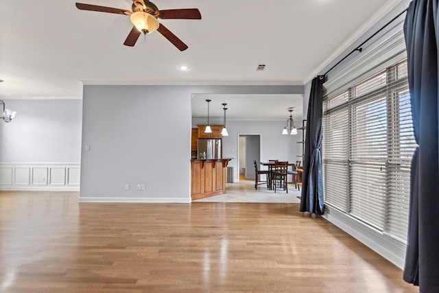 unfurnished living room featuring crown molding, ceiling fan with notable chandelier, and light hardwood / wood-style flooring