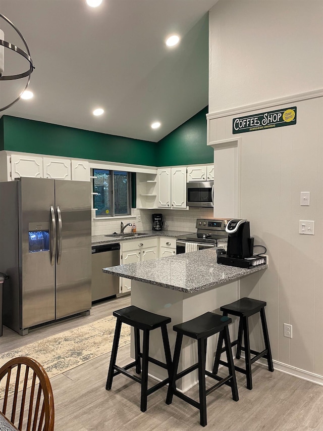 kitchen featuring appliances with stainless steel finishes, a breakfast bar, white cabinetry, sink, and light hardwood / wood-style flooring