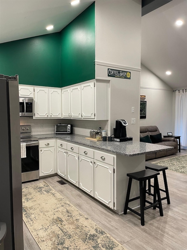 kitchen with appliances with stainless steel finishes, a breakfast bar, high vaulted ceiling, and white cabinets