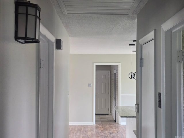 hallway with light wood finished floors, a textured ceiling, and baseboards