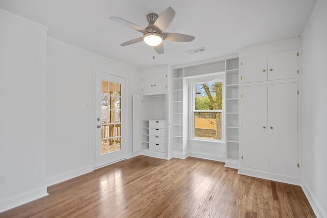 empty room featuring hardwood / wood-style flooring, ceiling fan, built in features, and a wealth of natural light