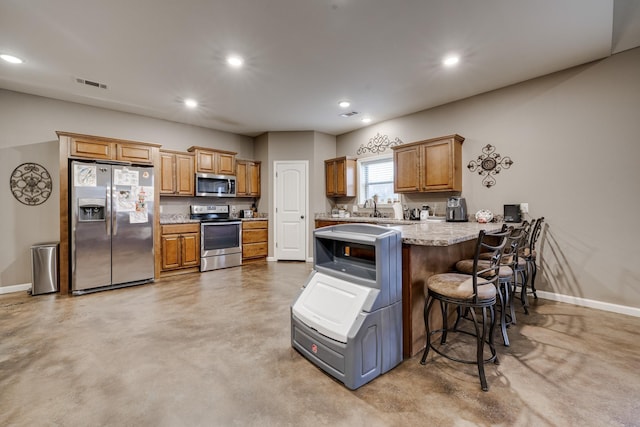 kitchen with sink, a breakfast bar area, light stone counters, kitchen peninsula, and stainless steel appliances