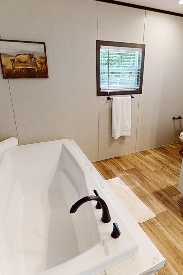 full bathroom featuring toilet, wood finished floors, and a tub to relax in