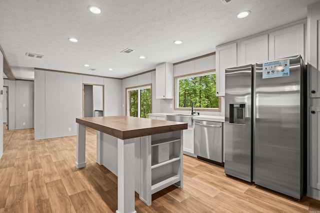 kitchen featuring stainless steel appliances, wood counters, white cabinets, a sink, and light wood finished floors