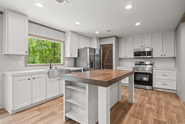 kitchen featuring appliances with stainless steel finishes, a sink, butcher block countertops, open shelves, and white cabinetry