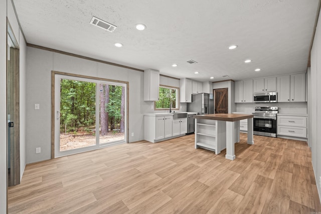 kitchen with appliances with stainless steel finishes, wood counters, recessed lighting, light wood-type flooring, and white cabinets