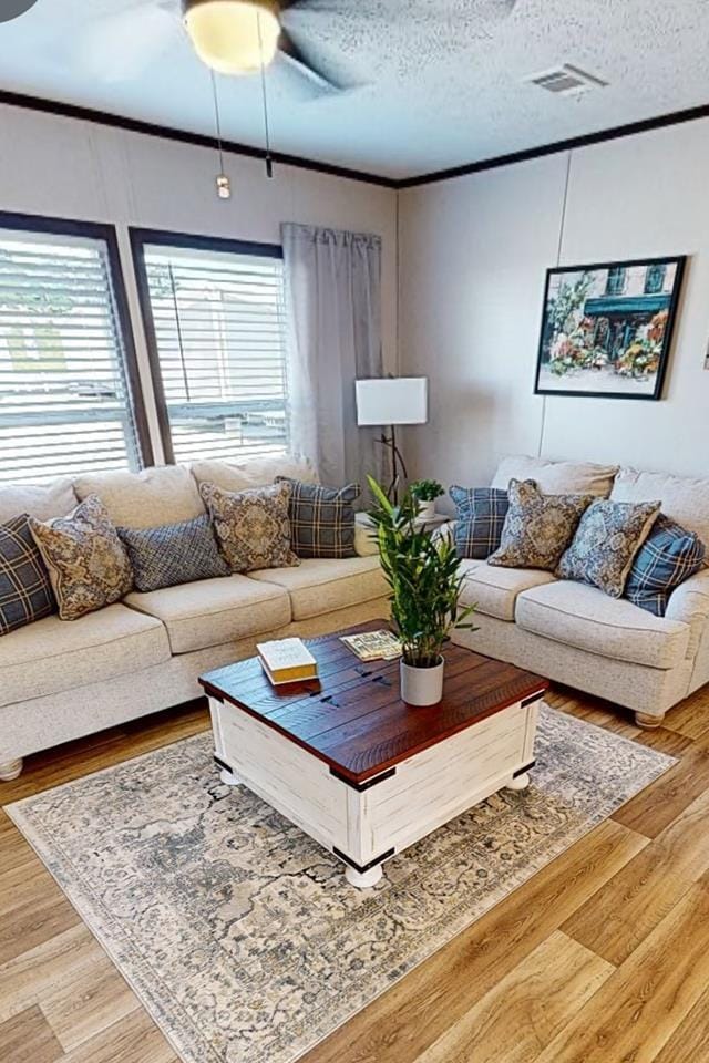 living area with crown molding, a ceiling fan, wood finished floors, and a textured ceiling