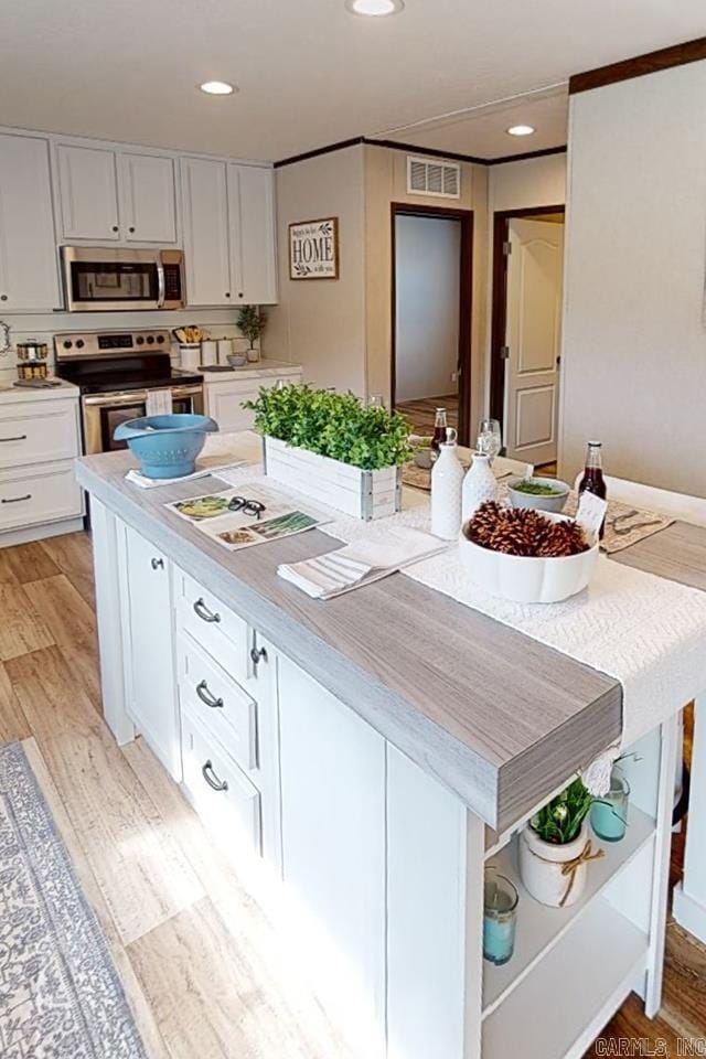 kitchen featuring appliances with stainless steel finishes, recessed lighting, white cabinets, light countertops, and a kitchen island