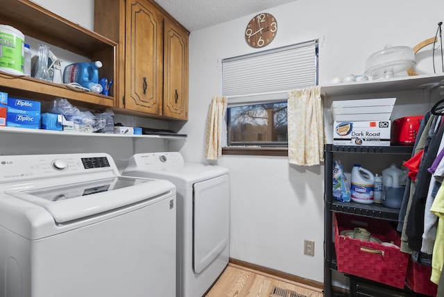 clothes washing area featuring cabinets, washing machine and clothes dryer, a textured ceiling, and light hardwood / wood-style flooring