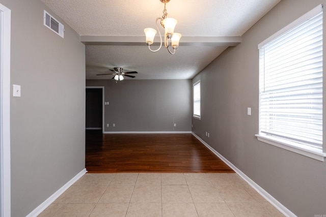 tiled empty room with ceiling fan with notable chandelier and a textured ceiling