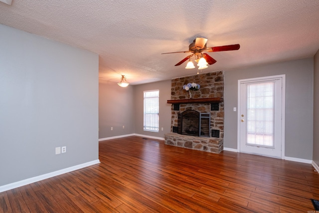 unfurnished living room with ceiling fan, a stone fireplace, dark hardwood / wood-style floors, and a textured ceiling