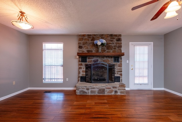 unfurnished living room with ceiling fan, a stone fireplace, dark hardwood / wood-style floors, and a textured ceiling