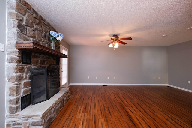 unfurnished living room featuring ceiling fan, a stone fireplace, wood-type flooring, and a textured ceiling