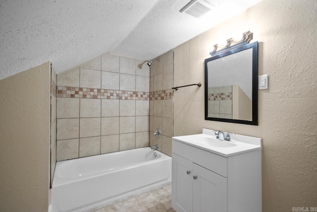 bathroom featuring vanity, tiled shower / bath combo, vaulted ceiling, and a textured ceiling