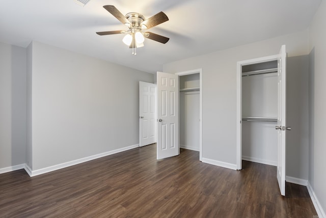 unfurnished bedroom featuring ceiling fan, dark hardwood / wood-style flooring, and two closets