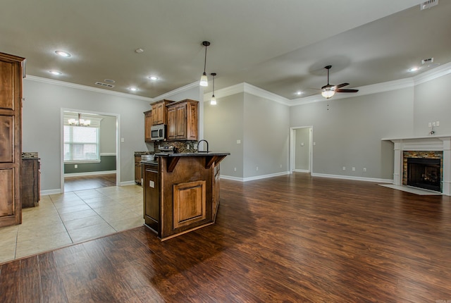 kitchen with a stone fireplace, a breakfast bar area, dark hardwood / wood-style flooring, ceiling fan with notable chandelier, and backsplash