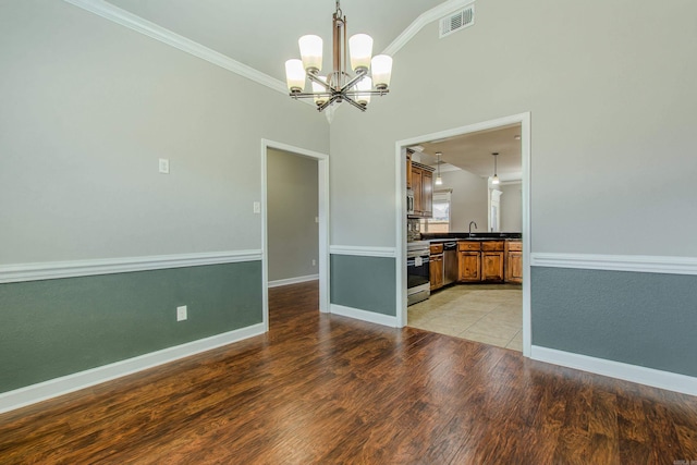 empty room with a notable chandelier, ornamental molding, sink, and light wood-type flooring