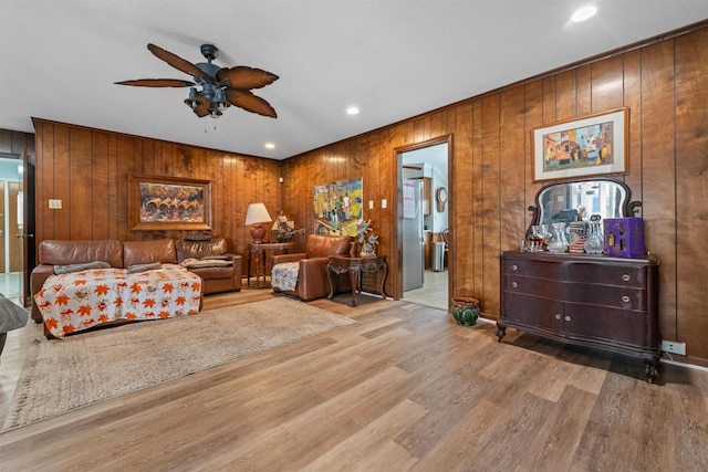 living room with ceiling fan, wooden walls, and light hardwood / wood-style floors