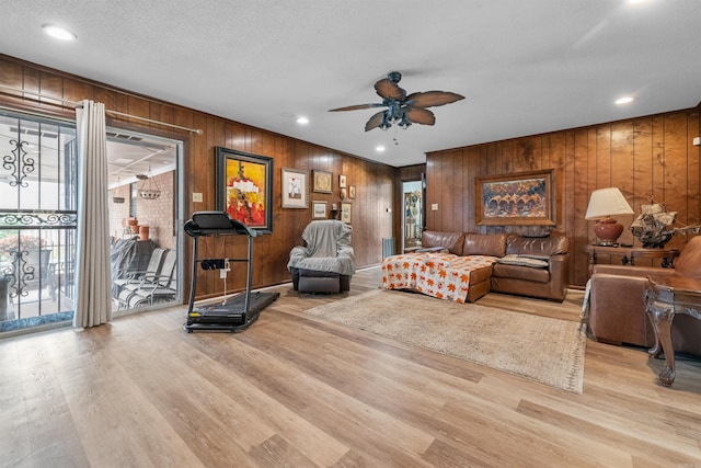 living room with ceiling fan, wooden walls, light hardwood / wood-style flooring, and a textured ceiling