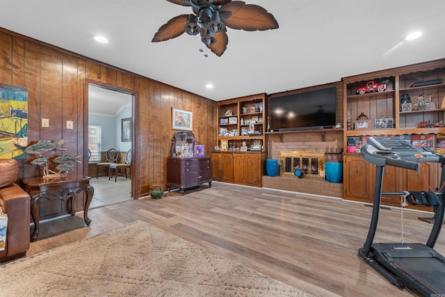 workout room with ceiling fan, ornamental molding, wooden walls, and light wood-type flooring