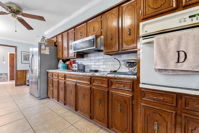 kitchen featuring appliances with stainless steel finishes, backsplash, ornamental molding, light tile patterned floors, and ceiling fan