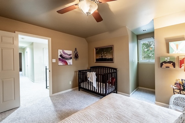 carpeted bedroom with a crib and ceiling fan