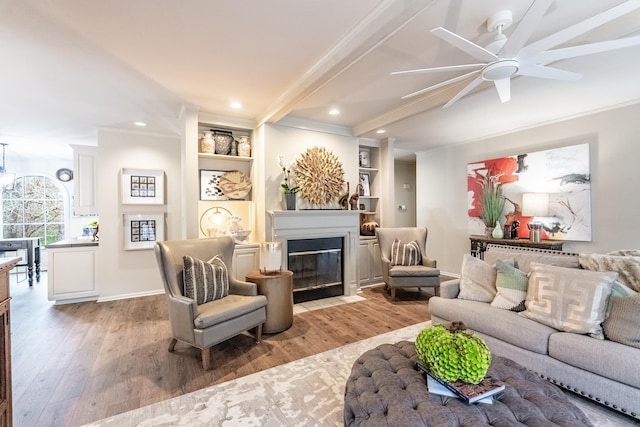 living room with crown molding, built in shelves, light hardwood / wood-style flooring, and beamed ceiling