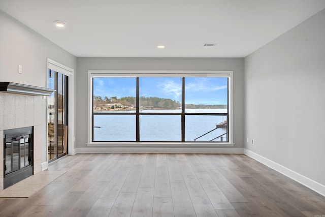 unfurnished living room featuring a tiled fireplace, light hardwood / wood-style floors, and a water view