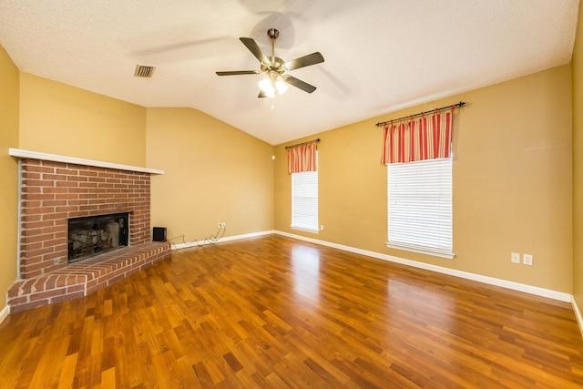 unfurnished living room featuring hardwood / wood-style flooring, vaulted ceiling, a brick fireplace, and a textured ceiling