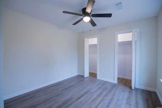 unfurnished bedroom featuring dark hardwood / wood-style flooring, a spacious closet, a closet, and ceiling fan