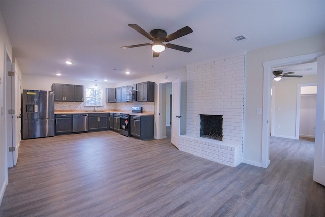 kitchen with sink, light hardwood / wood-style flooring, backsplash, stainless steel appliances, and a fireplace