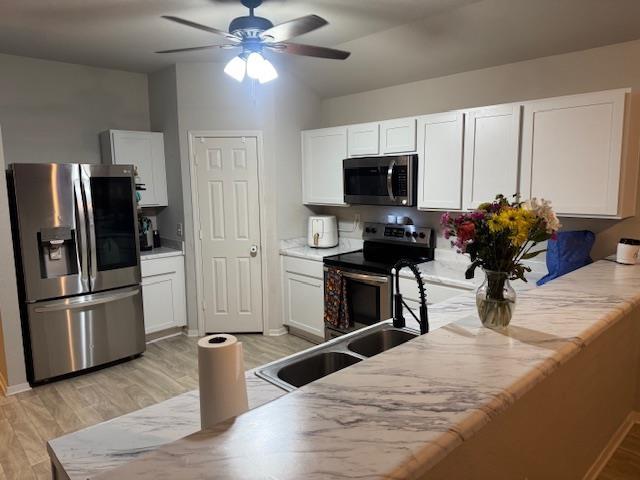 kitchen with appliances with stainless steel finishes, white cabinetry, sink, ceiling fan, and light hardwood / wood-style flooring