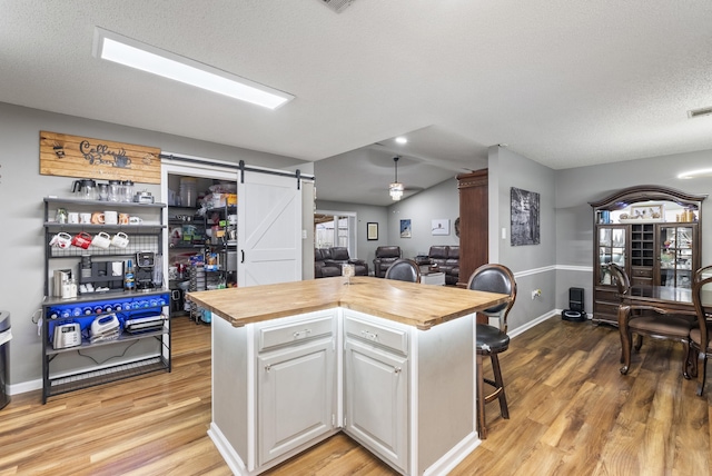 kitchen with butcher block counters, a breakfast bar area, white cabinetry, a center island, and a barn door