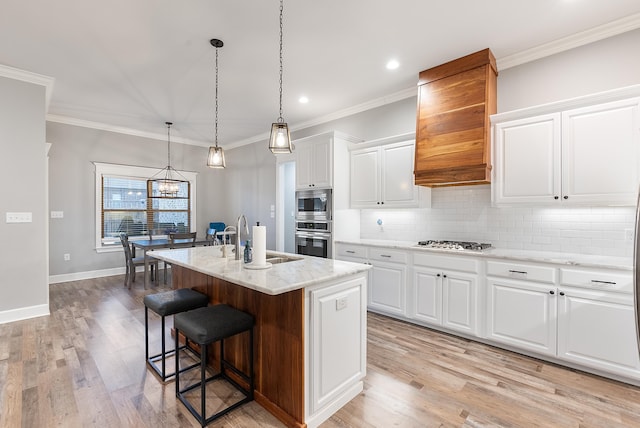 kitchen featuring pendant lighting, sink, white cabinets, a kitchen island with sink, and light stone counters