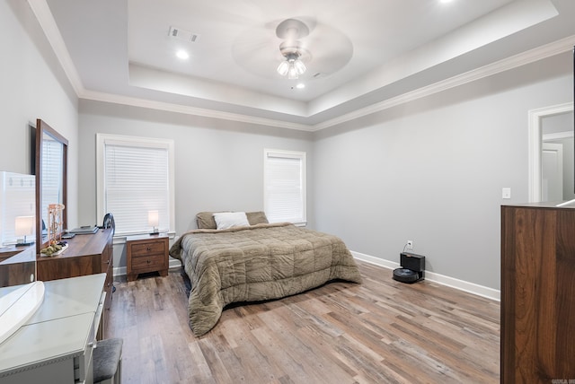 bedroom with ornamental molding, ceiling fan, light wood-type flooring, and a tray ceiling