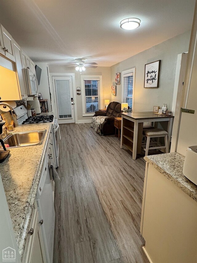 kitchen featuring white cabinetry, sink, light stone counters, white appliances, and light hardwood / wood-style flooring