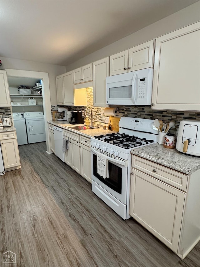 kitchen featuring sink, white appliances, washer and clothes dryer, hardwood / wood-style flooring, and backsplash