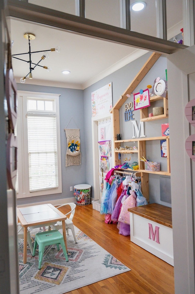 playroom featuring wood-type flooring, ornamental molding, and a chandelier