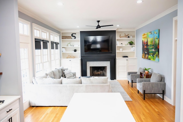 living room with crown molding, a fireplace, built in shelves, and light hardwood / wood-style flooring