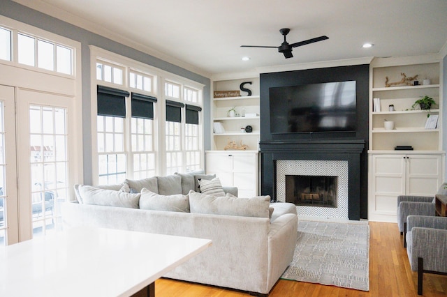 living room with ornamental molding, built in features, ceiling fan, a fireplace, and light hardwood / wood-style floors