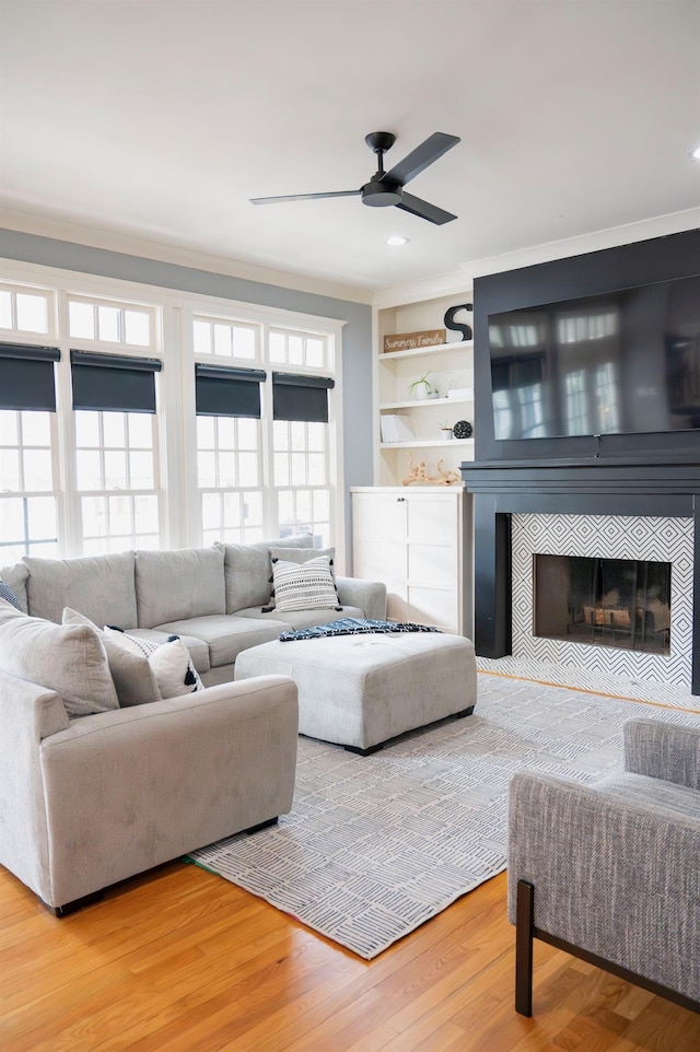 living room featuring crown molding, ceiling fan, a fireplace, wood-type flooring, and built in shelves