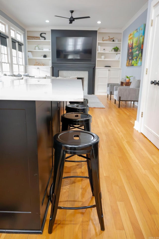 kitchen with ceiling fan, built in features, a breakfast bar, and light hardwood / wood-style flooring