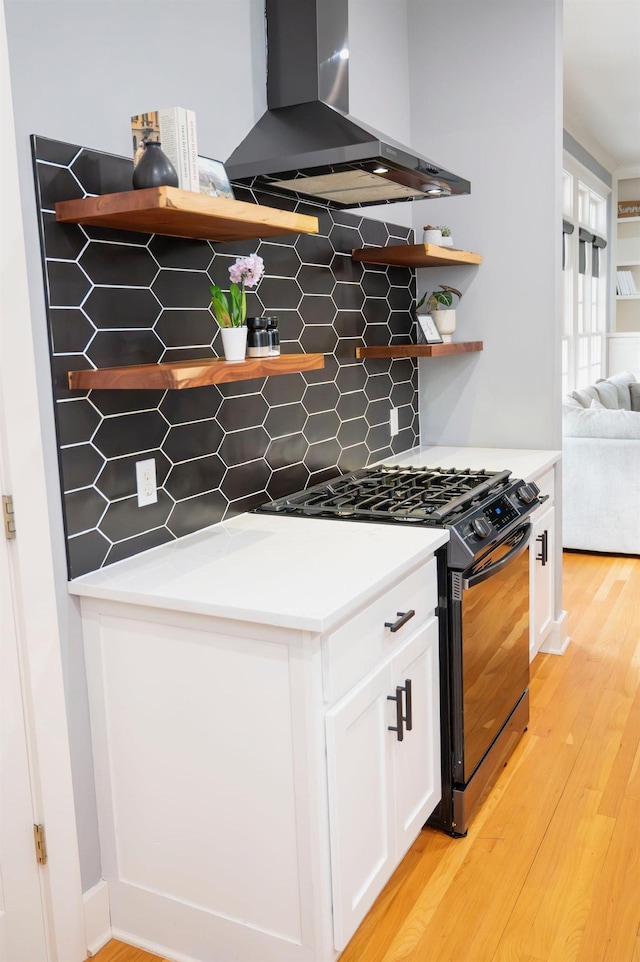 kitchen with white cabinetry, tasteful backsplash, black range with gas stovetop, light hardwood / wood-style floors, and exhaust hood