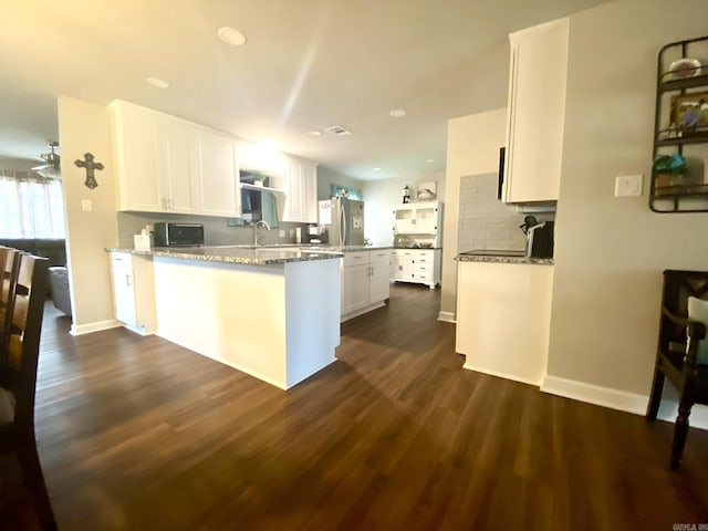 kitchen with stainless steel refrigerator, dark hardwood / wood-style floors, light stone countertops, white cabinets, and kitchen peninsula