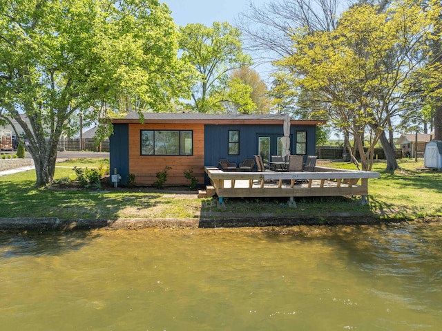 back of house with a deck with water view and a lawn